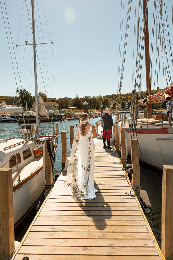 Bride walking up to her groom next to the sailboat for him to see her for the first time and his back is turned 