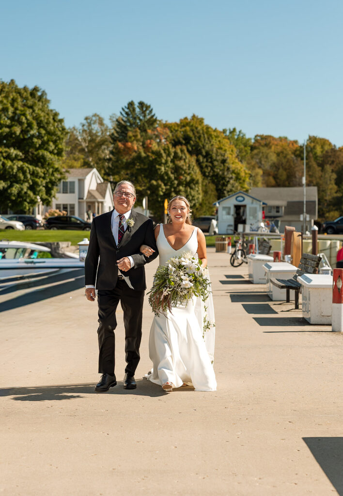 Bride coming down the dock being walked by her dad holding her bouquet