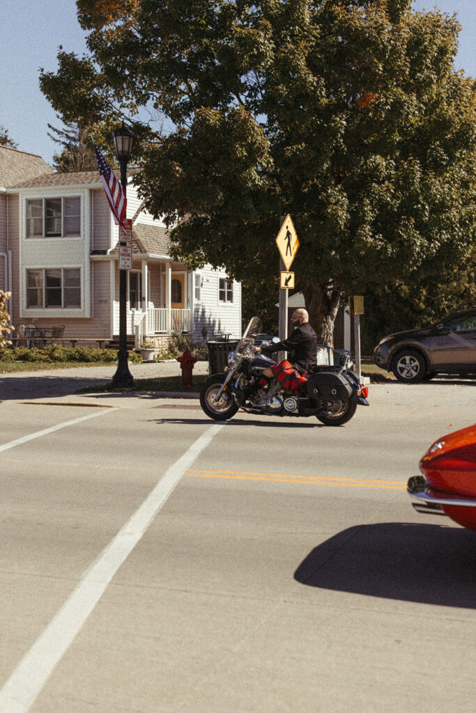 Groom driving his motorcycle in downtown Sister Bay, on his way to his sailboat wedding ceremony
