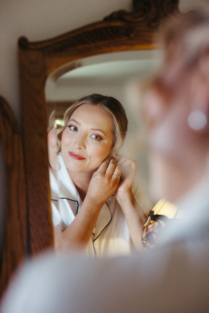 Bride putting on her earring while getting ready in her room before an intimate Door County sailboat wedding