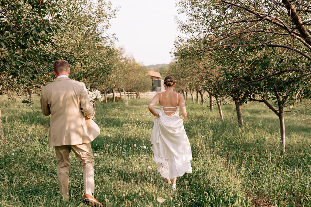 Bride and groom run together through trees during their Door County wedding portraits
