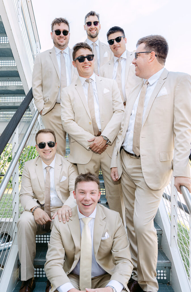 Groom and groomsmen laughing together on the stairs before a wedding at the Kress Pavilion