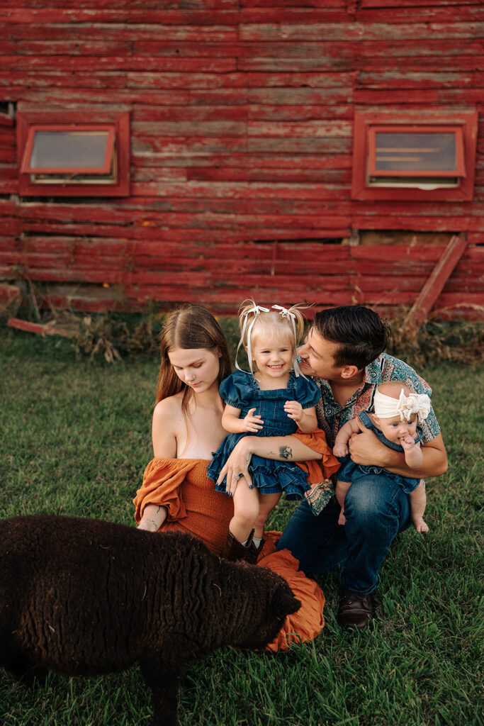 Family sitting together on a farm during a fall family photo session in Door County, Wisconsin, with children interacting naturally and animals nearby.